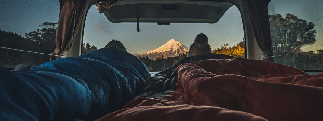 People laying in back of campervan in sleeping bags