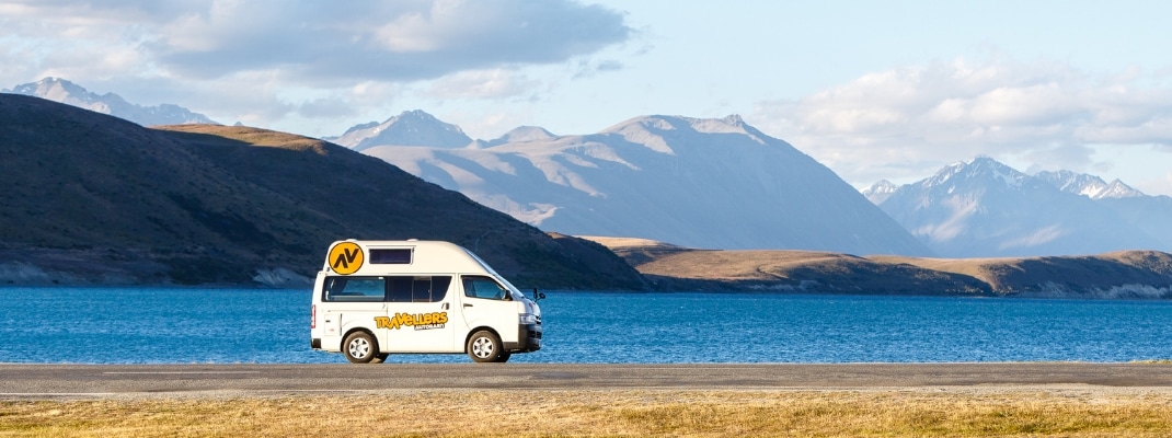 Campervan parked on side of road with view of lake and mountains, New Zealand. 
