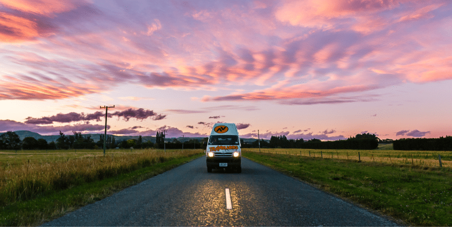 Campervan driving on road in New Zealand with colourful sunset