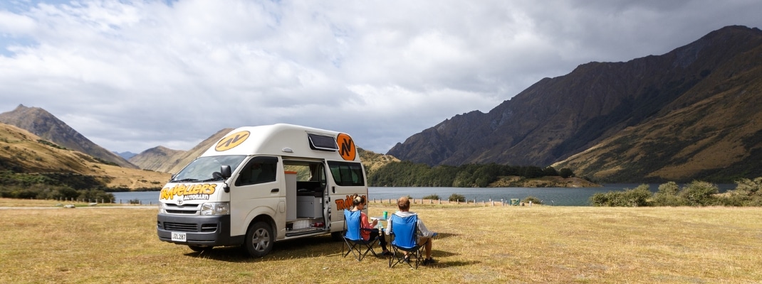 People sitting next to campervan parked with mountain views, New Zealand 