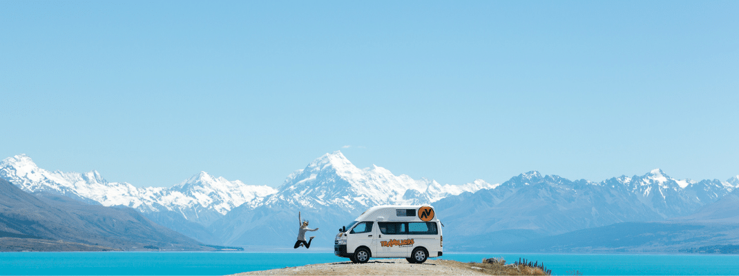 Person jumping next to campervan with mountain backdrop, New Zealand