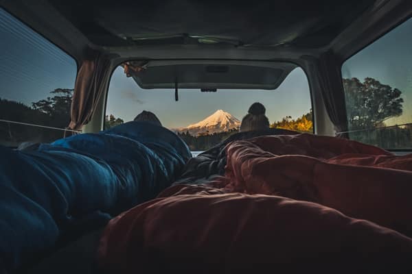Two people laying in the back of campervan looking at mountains in New Zealand - Buying a Campervan in New Zealand