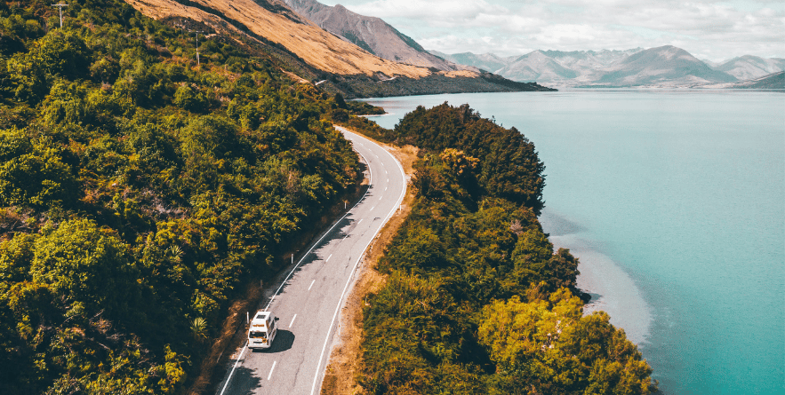Campervan driving along road next to lake in New Zealand