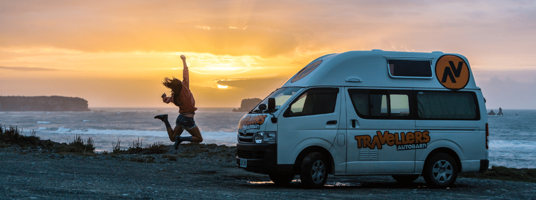 Person jumping next to campervan next to beach 