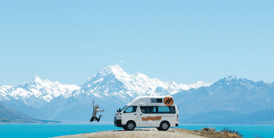 Person jumping next to campervan with view of New Zealand lake and mountains