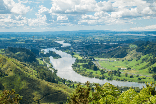 Panoramic view on river valley with lush green and river flowing through the shot during sunny day with blue sky and some clouds. On the picture is Waikato, longest river in New Zealand.